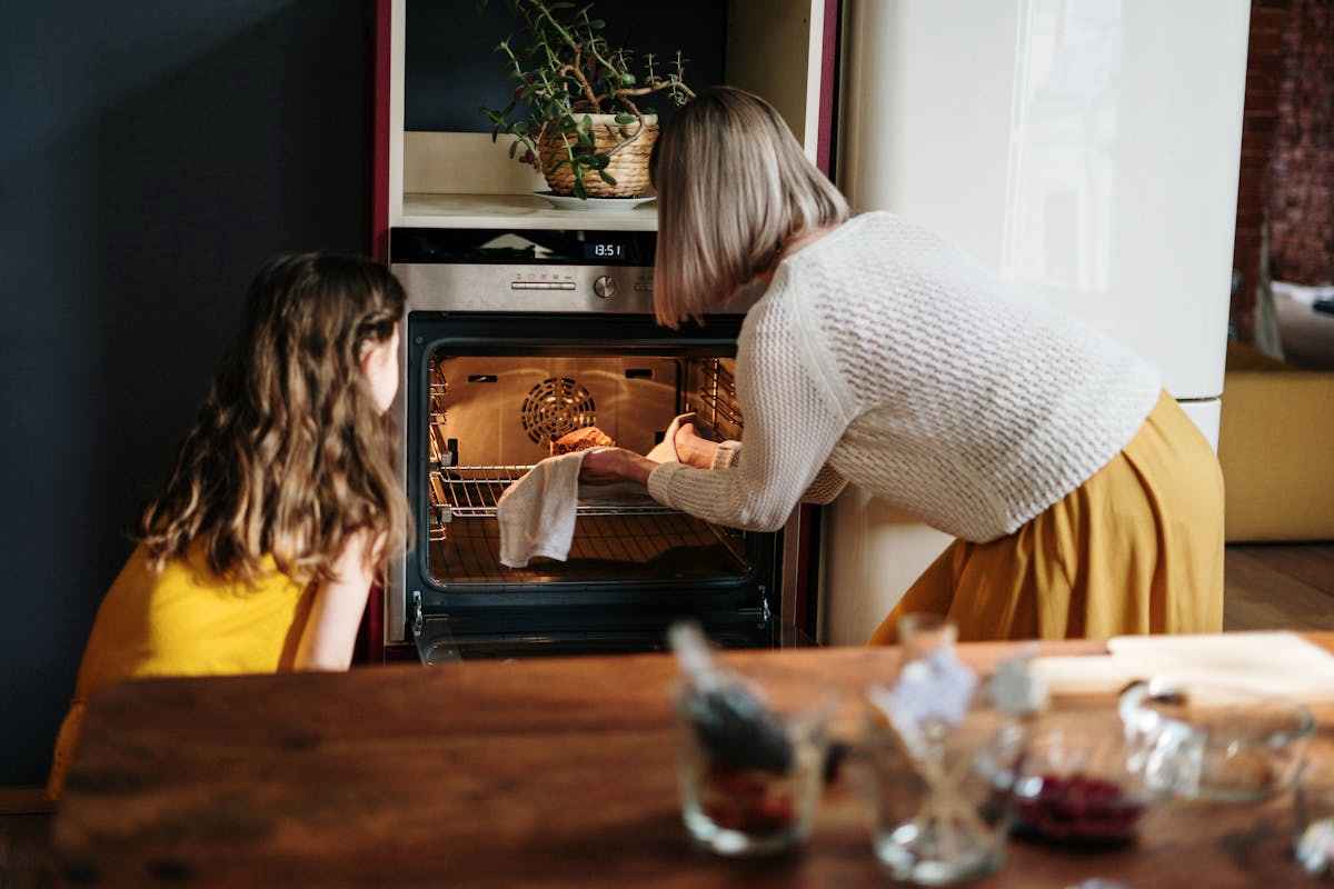 Donna e bambina che mettono una teglia in forno